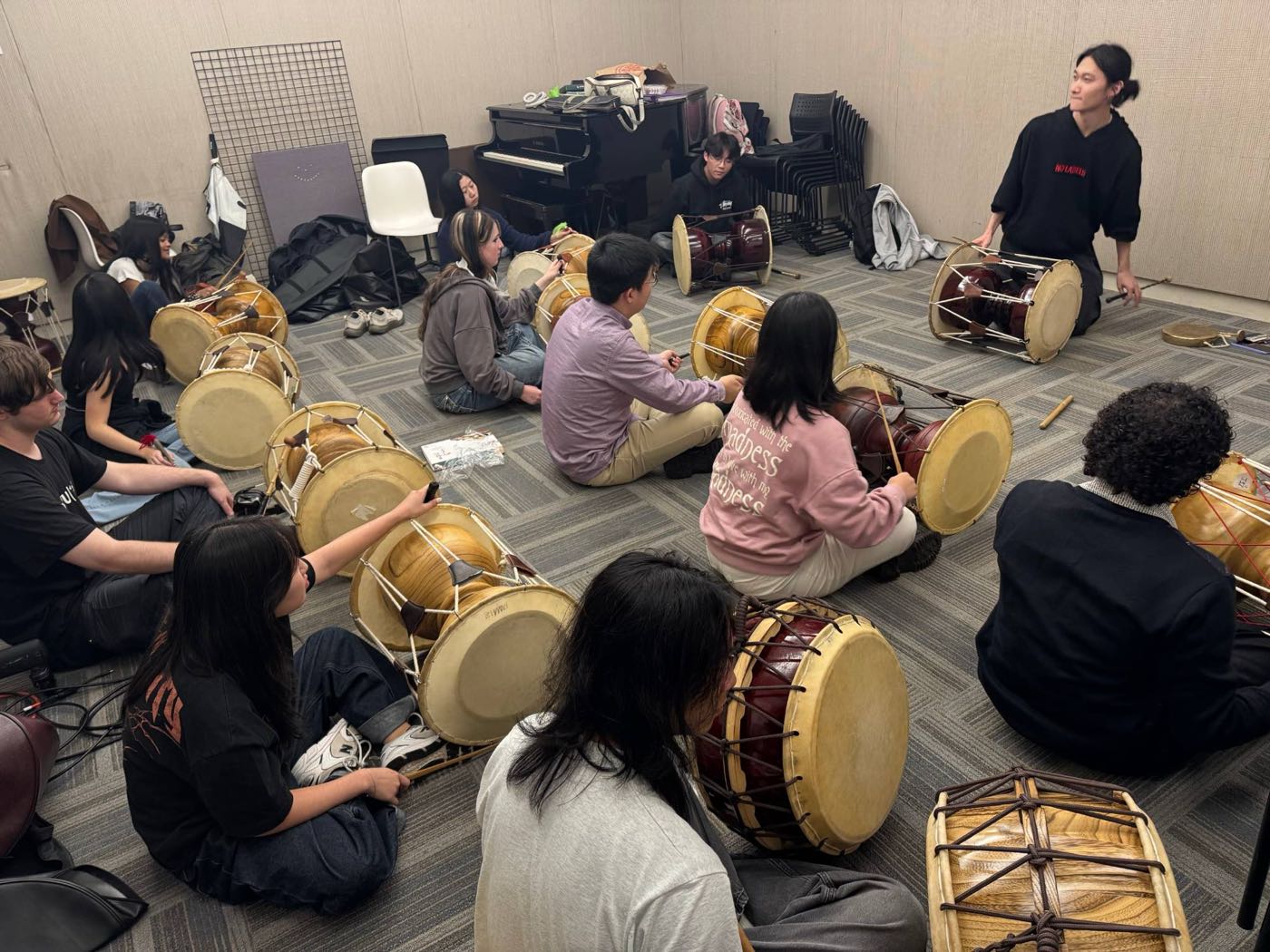 Members seated in a circle on the floor with janggu, learning a rhythm