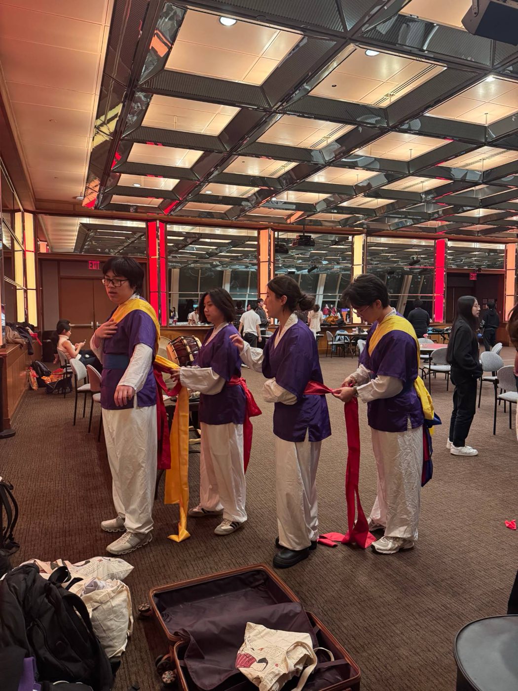 Members in purple and white performance outfits tying each other's sashes before a show