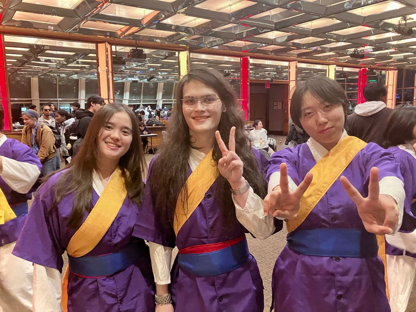 Three members in performance outfits smiling and throwing peace signs