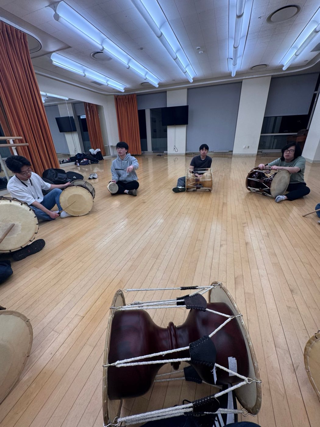 Members seated in a circle with janggu and buk, one leading the rhythm